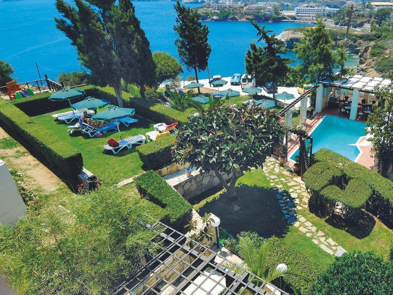 Pohled na hotelovou oblast s bazénem, lehátky a mořem v pozadí.