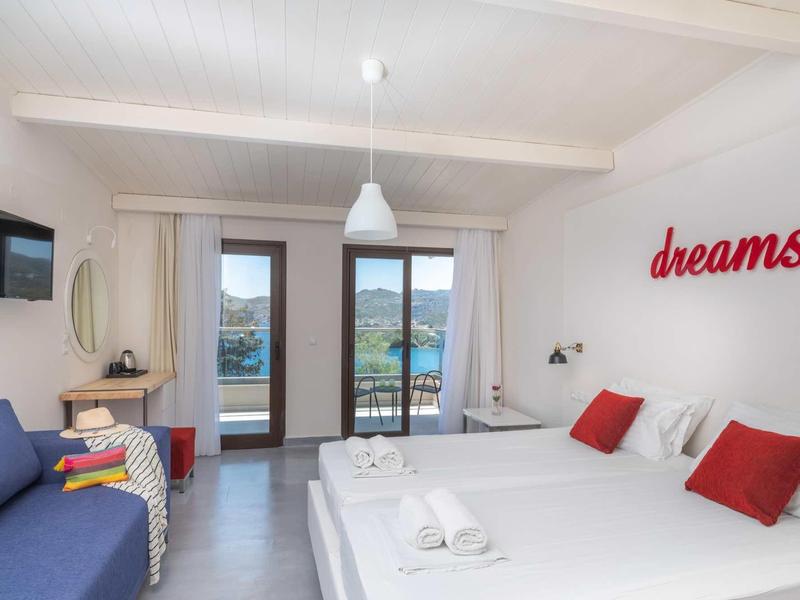 Světý hotelový pokoj se dvěma postelemi, modrou pohovkou a výhledem na bazén přes velká okna.