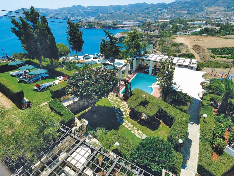 Pohled na zahradu s bazénem, lehátky a mořem s horami v pozadí.