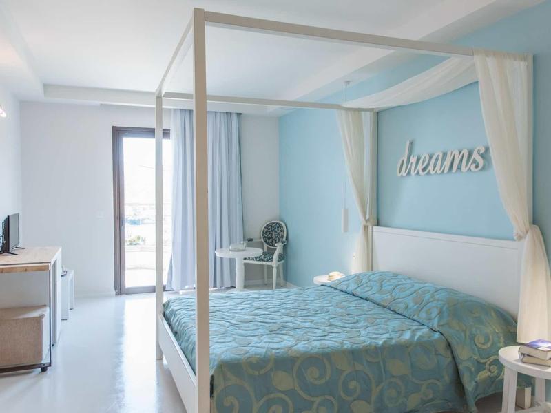 Světle zařízená ložnice s postelí s nebesy, modrou zdí a koupelnou v pozadí.