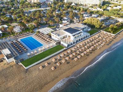 Ośrodek nadmorski z basenem, leżakami i palmami przy morzu.