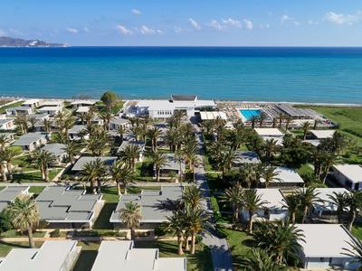 Widok na ośrodek hotelowy z bungalowami, palmami i basenem nad morzem pod niebieskim niebem.