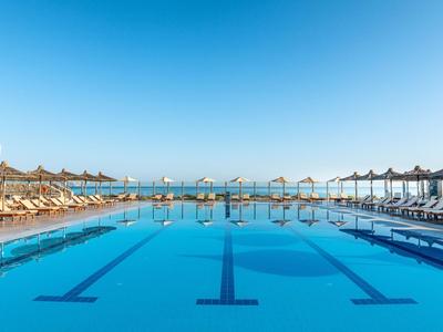 Duży basen na zewnątrz z parasolami i leżakami pod czystym niebem nad morzem.