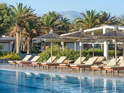 Leżaki przy basenie z parasolami, na tle tropikalnej roślinności i gór w tle.