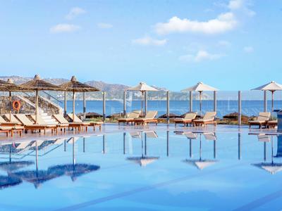 Basen infinity z leżakami i parasolami z widokiem na morze i niebo.