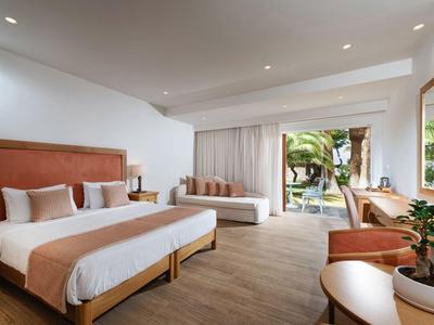 Jasny pokój hotelowy z dwoma łóżkami, drewnianą podłogą i dostępem do tarasu z widokiem na ogród.