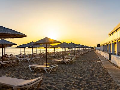 Sandstrand mit Reihen von Sonnenliegen und Sonnenschirmen bei Sonnenaufgang am Meer.
