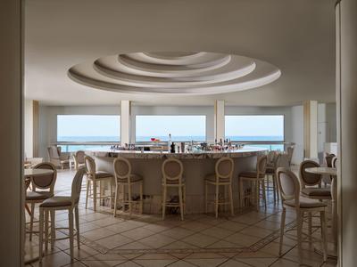 Moderní kruhový bar s výhledem na moře a elegantním stropem v světlé místnosti.