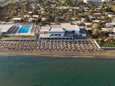 Luxusní hotel s bazénem a lehátky na klidné pláži u modrého moře v letovisku.