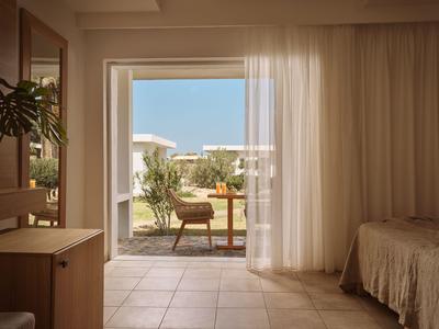 Hotelzimmer mit Blick auf eine Terrasse und Garten unter blauem Himmel.