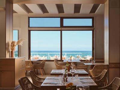 Světle zařízená restaurace s výhledem na moře a prostřenými stoly.