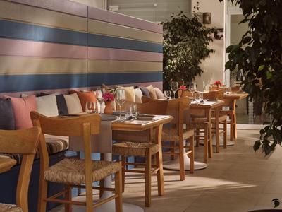Moderner Hotelrestaurantbereich mit Holztischen, farbigen Polstern und Pflanzen.