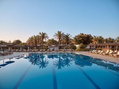 Großer Pool mit Liegestühlen und Palmen unter klarem Himmel in einem Hotelresort.