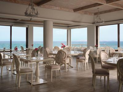 Helles Restaurant mit weißen Stühlen und Tischen, großer Fensterfront mit Meerblick.