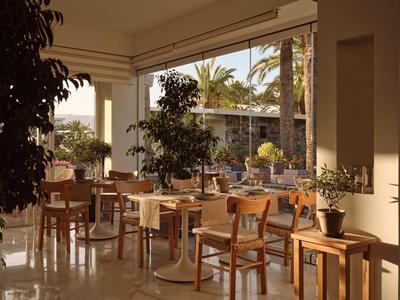 Offener Hotelterrassenbereich mit Holzstühlen, Tischen und Pflanzen bei Tageslicht.