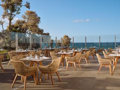 Terrasse mit Holzstühlen vor Meerblick bei klarem Himmel am Hotel.