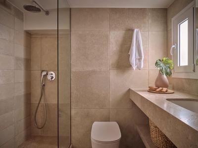Modernes Badezimmer mit Regenwalddusche, Toilette und Naturstein-Oberflächen in warmen Tönen.