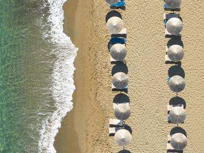 Widok z lotu ptaka na piaszczystą plażę z rzędami parasoli i turkusową wodą