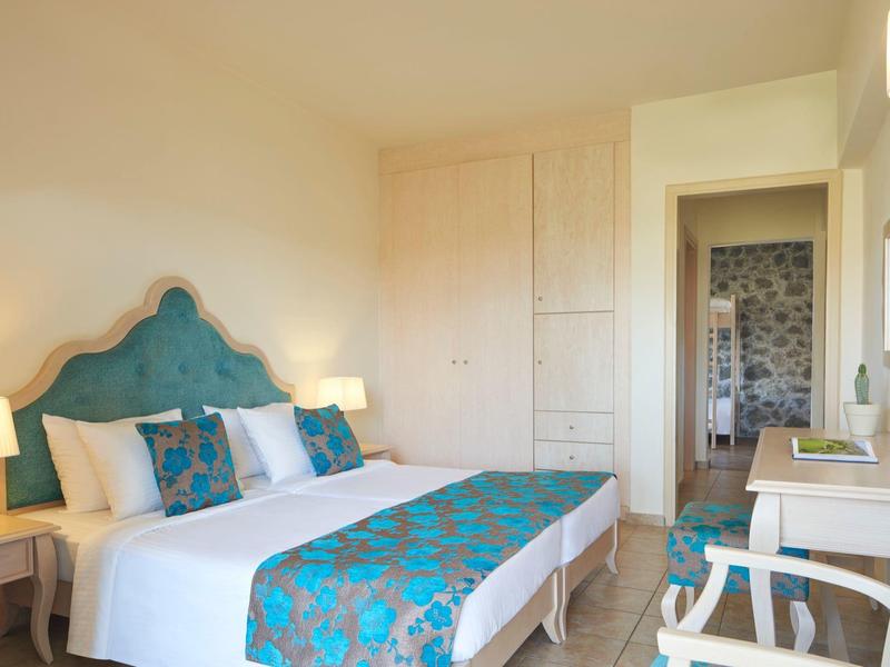 Jasny pokój hotelowy z dużym łóżkiem, turkusowymi akcentami i miejscem do pracy.