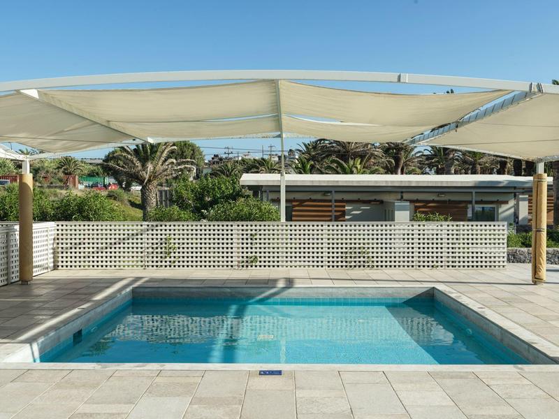 Nowoczesny prostokątny basen z krystalicznie czystą wodą pod daszkiem przeciwsłonecznym obok ogrodu.