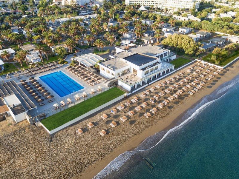 Ośrodek nadmorski z basenem, leżakami i palmami przy morzu.