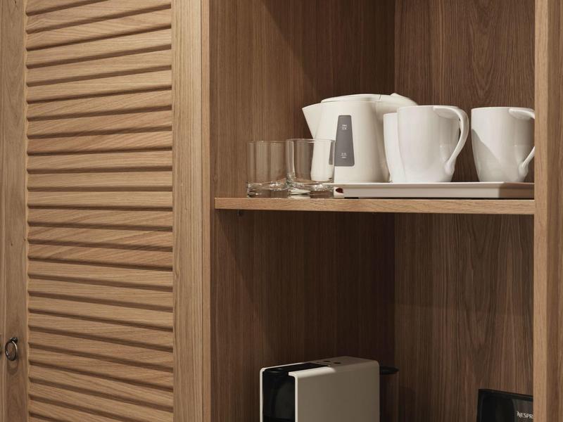 Drewniana półka z czajnikiem, filiżankami i akcesoriami do kawy w pokoju hotelowym