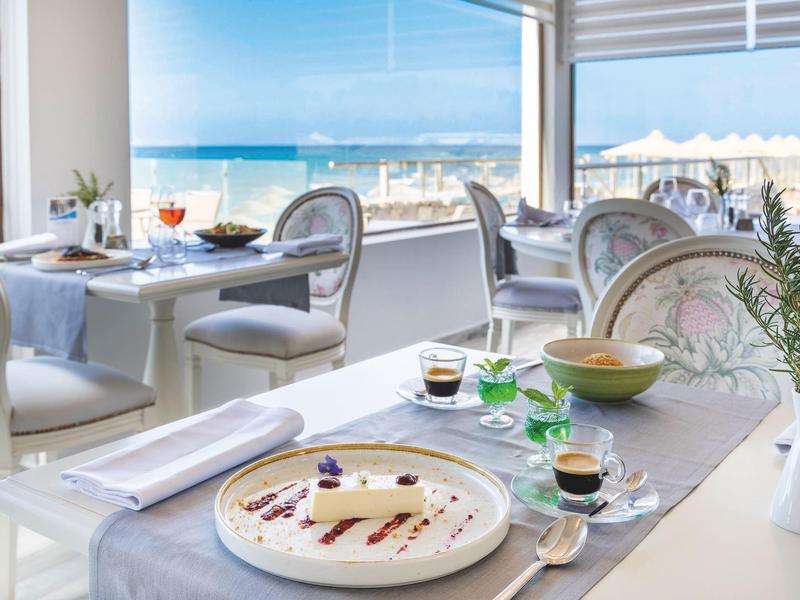 Nowoczesna restauracja z widokiem na morze, elegancko nakryte stoły i wygodne krzesła.