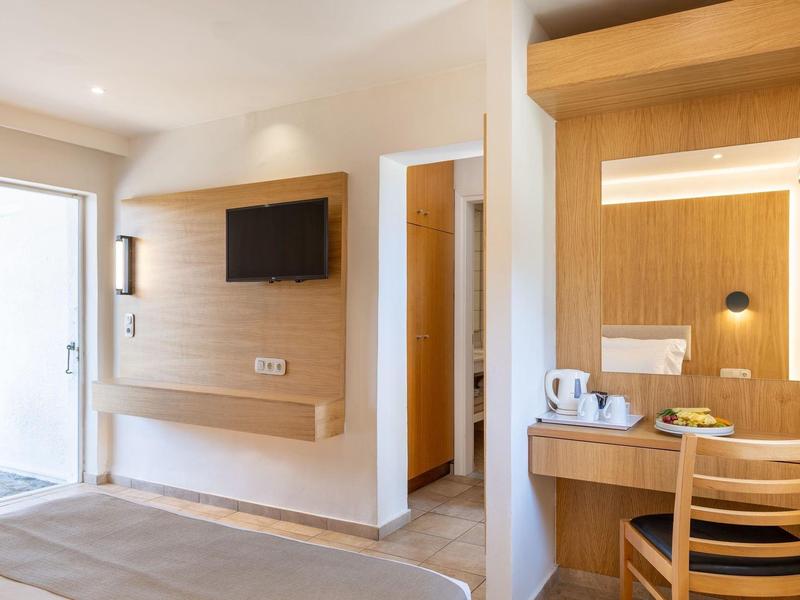 Jasny pokój hotelowy z drewnianymi akcentami, biurkiem, krzesłem i telewizorem na ścianie.