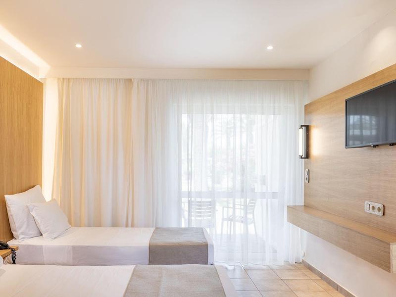 Jasny pokój hotelowy z dwoma pojedynczymi łóżkami, drewnianymi akcentami i telewizorem na ścianie.