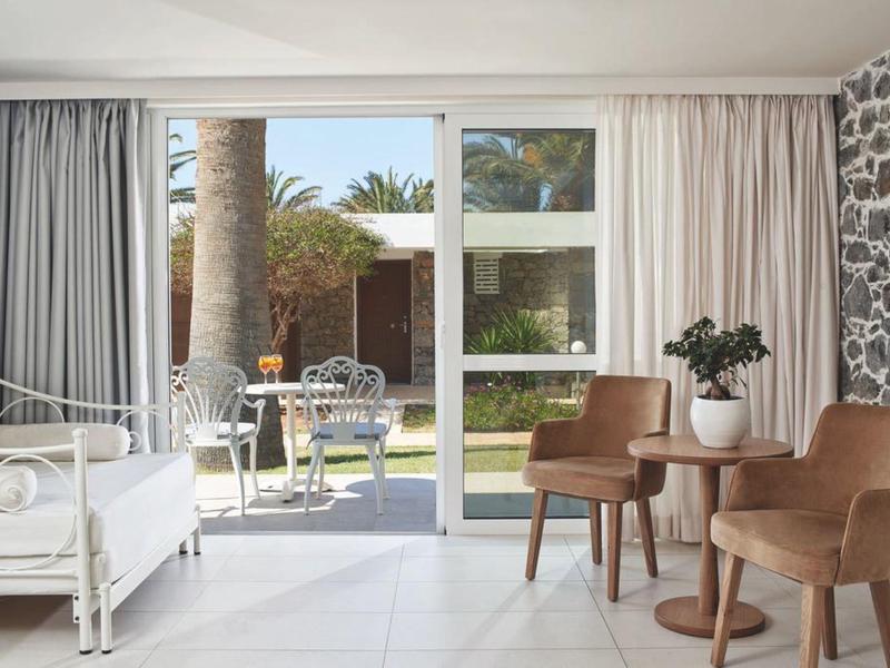 Jasny pokój hotelowy z białym łóżkiem, kamienną kolumną i miejscem do siedzenia z widokiem na patio i ogród.