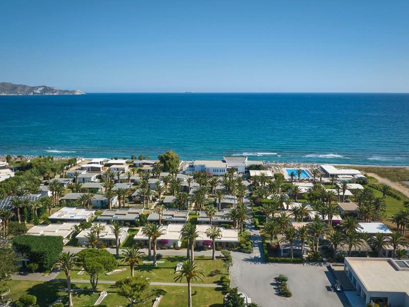 Widok na nadmorski ośrodek hotelowy z basenami, ogrodami i parkingami pod błękitnym niebem.