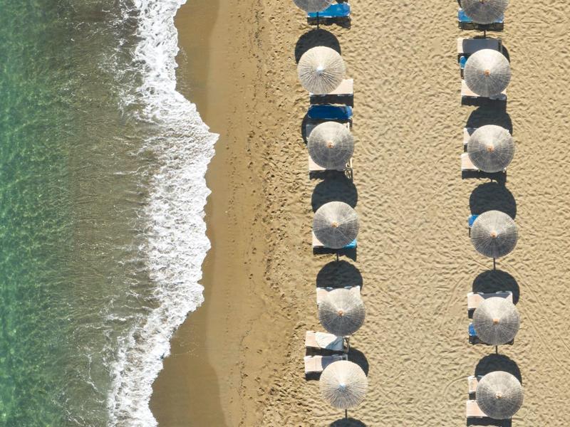 Widok z lotu ptaka na piaszczystą plażę z rzędami parasoli i turkusową wodą