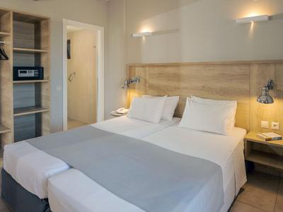 Habitación de hotel luminosa con cama doble, cabecero beige y armario abierto.