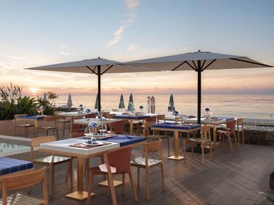 Terraza de restaurante con mesas y sombrillas junto al mar al atardecer.