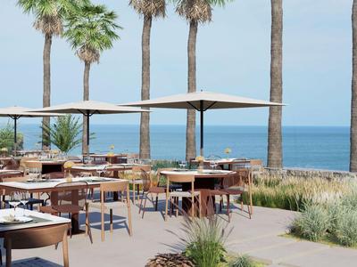 Restaurante al aire libre con mesas, sillas y sombrillas con vista al mar y palmeras