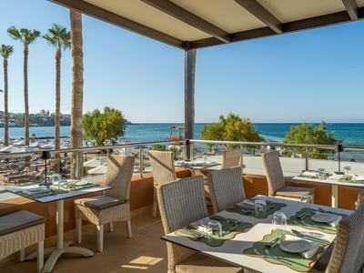 Freiluftrestaurant am Meer mit gedeckten Tischen und Blick auf Strand und Palmen.