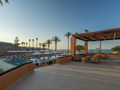 Große Terrasse mit Sitzbereich, Blick auf Pool, Liegestühle und Palmen im Sonnenuntergang.