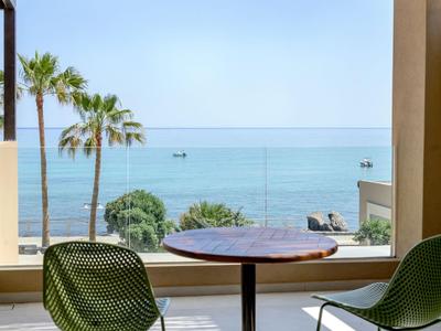 Blick von einem Hotelzimmer mit Tisch und Stühlen auf das Meer und Palmen.