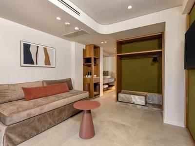 Modern eingerichtetes Hotelzimmer mit Sofa, kleinem Beistelltisch und offenem Kleiderschrank.
