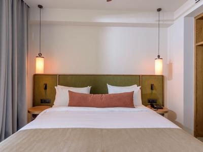 Ein modernes Hotelzimmer mit einem großen Bett, grüner Kopfteil und zwei hängenden Lampen.