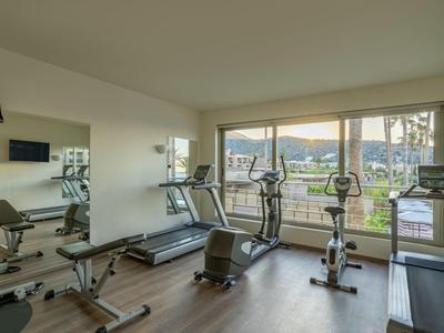Heller Fitnessraum mit Laufbändern, Fahrrädern und großen Fenstern mit Blick auf Bäume und Gebäude.