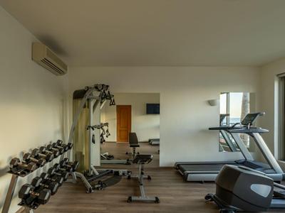 Kleiner Fitnessraum mit Hanteln, Geräten und Laufbändern, heller Raum mit Fenster.