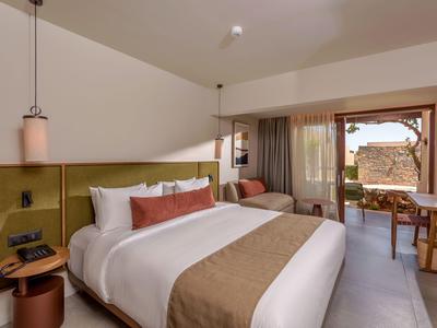 Modernes Hotelzimmer mit großem Bett, Sitzbereich und Blick auf Terrasse und Natur.