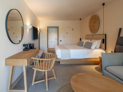 Modernes Hotelzimmer mit großem Bett, Schreibtisch, Holzstuhl und gemütlicher Sitzecke.