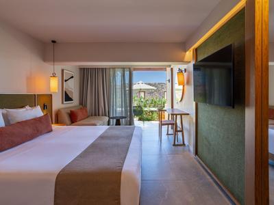Modernes Hotelzimmer mit Doppelbett, Sitzbereich und Blick auf einen Balkon mit Garten