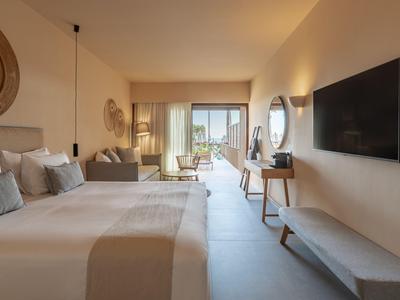Modern eingerichtetes Hotelzimmer mit Doppelbett, Sofa, Fernseher und Balkon mit Meerblick.