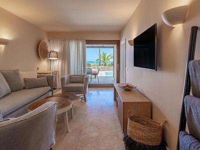 Modernes Hotelzimmer mit Sitzbereich, großem Fernseher und Blick auf Balkon mit Pool.