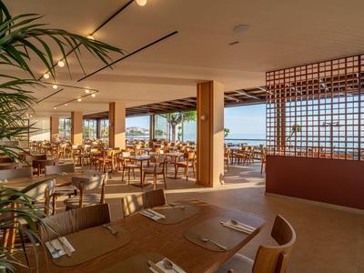 Helles, modern eingerichtetes Restaurant mit Holztischen und großen Fenstern mit Meerblick.