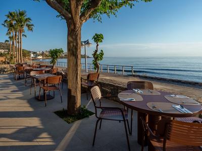 Terrasse mit Tischen und Stühlen am Meer unter blauem Himmel bei Sonnenaufgang.