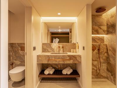 Modernes Hotelbad mit Marmorakzenten, begehbarer Dusche und Handtüchern auf Ablage.